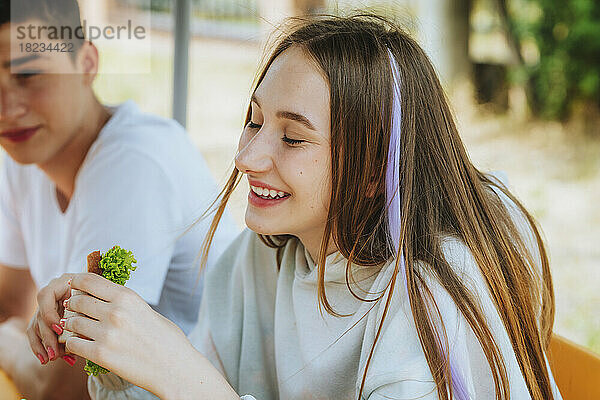 Fröhliches Teenager-Mädchen isst Sandwich mit Freunden auf dem Schulhof