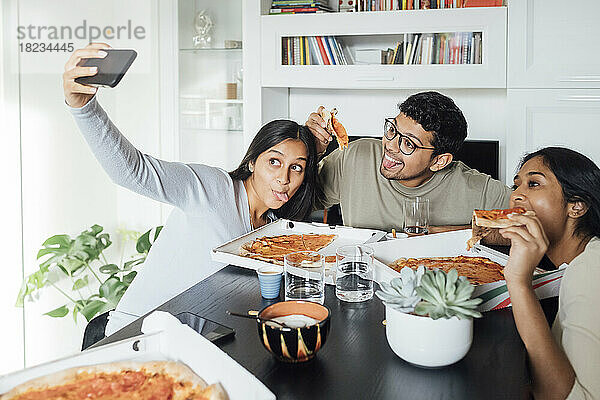 Junge Frau macht Selfie mit dem Handy  während Frau und Mann zu Hause Pizza essen