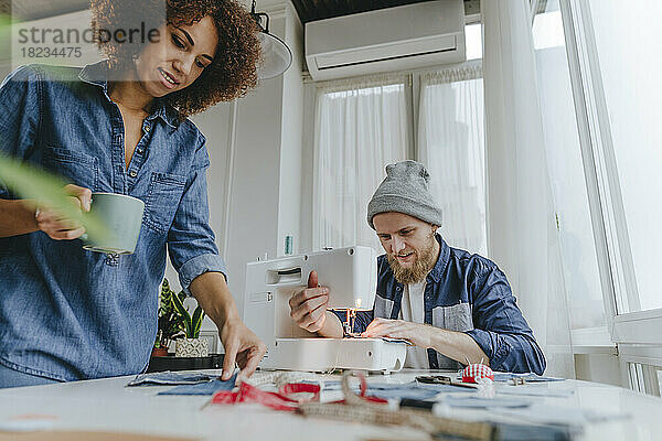 Modedesigner arbeitet an Nähmaschine  während Kollege Stoff in Werkstatt untersucht