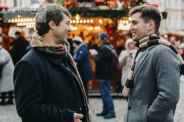 Lächelnder reifer Mann im Gespräch mit seinem Sohn  der auf dem Weihnachtsmarkt steht