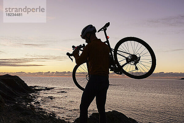 Radfahrer mit Fahrrad vor dem Meer bei Sonnenaufgang