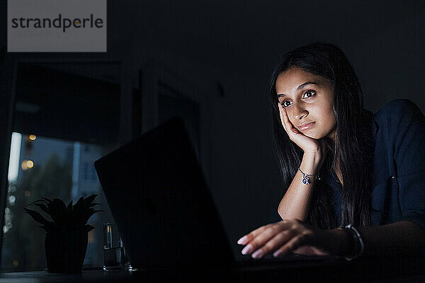 Frau mit Kopf in der Hand schaut auf Laptop
