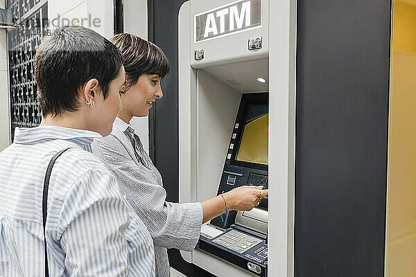 Junge Frau mit Freundin benutzt Geldautomaten