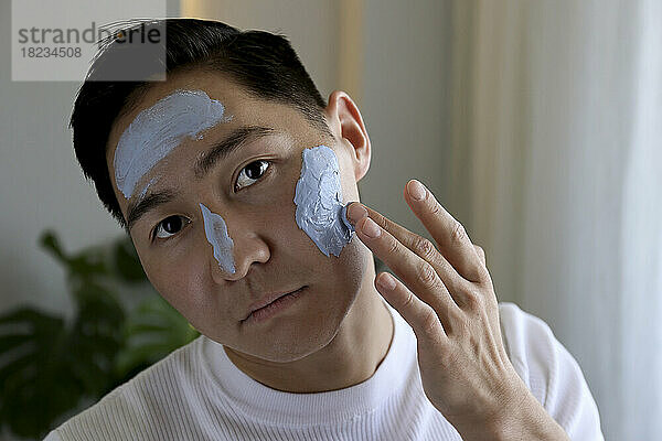 Young man applying mask on face at home