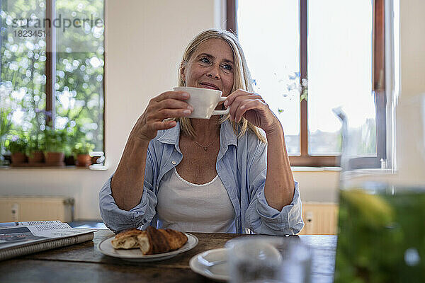 Thoughtful mature woman with coffee cup sitting at table