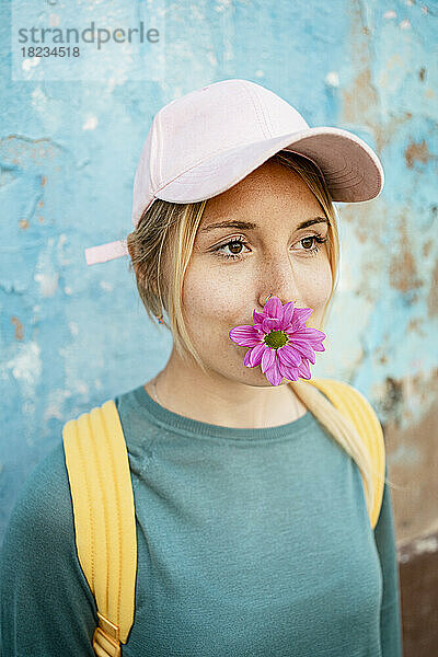 Nachdenkliche junge Frau hält Blume im Mund