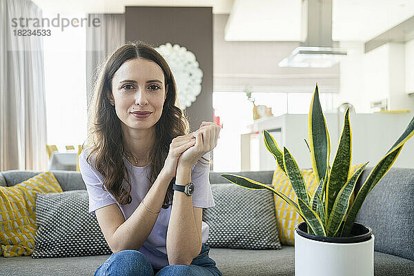 Lächelnde Frau sitzt zu Hause auf dem Sofa im Wohnzimmer