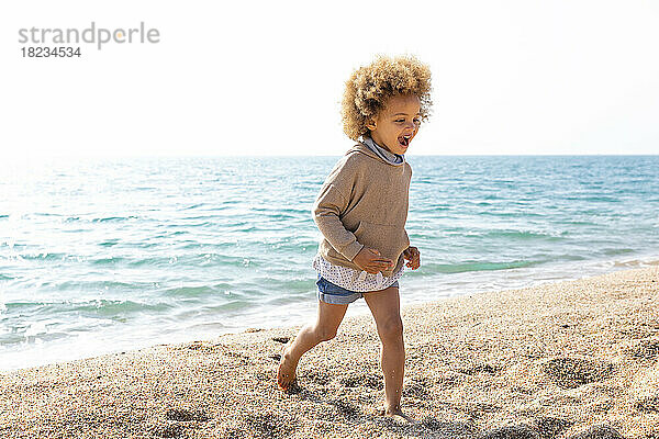 Fröhliches Mädchen läuft am Strand vor dem Meer