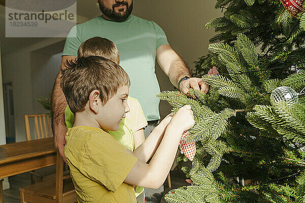 Vater hilft Söhnen beim Schmücken des Weihnachtsbaums zu Hause