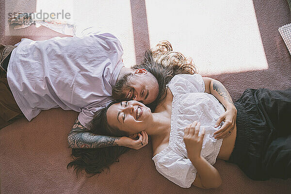 Cheerful hipster couple lying on bed at home