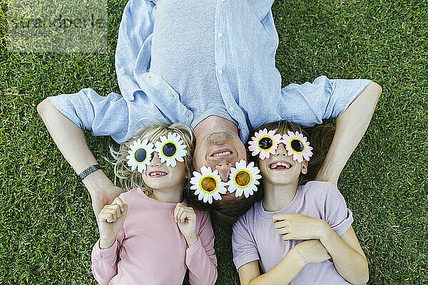 Happy father and daughters wearing flower sunglasses relaxing in grass