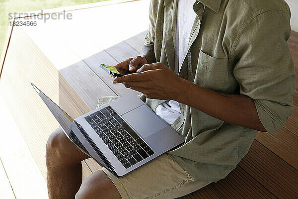 Hands of freelancer using smart phone sitting with laptop on lap