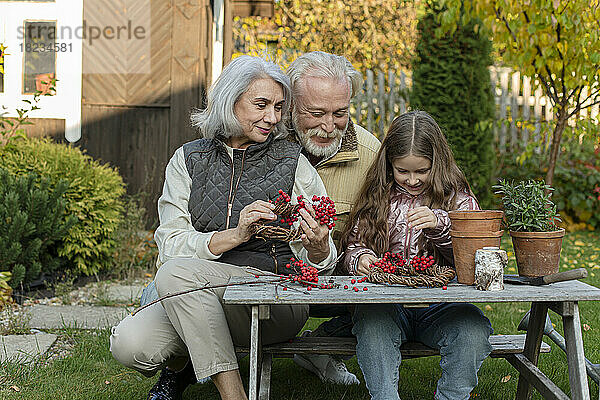 Großeltern und Enkelin sitzen am Gartentisch und basteln mit Eberesche