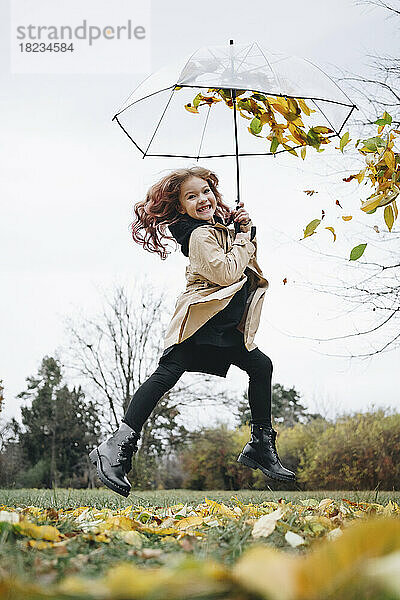 Fröhliches süßes Mädchen  das mit Regenschirm im Park springt