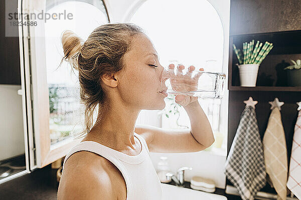 Frau trinkt Wasser aus einem Glas in der Küche