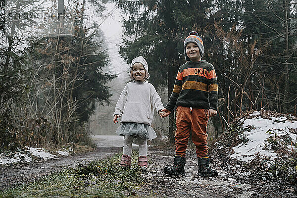 Glückliche Geschwister halten sich an den Händen und stehen im Wald
