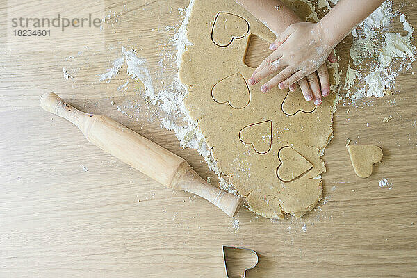 Hands of girl cutting cookie dough with cutter on table at home