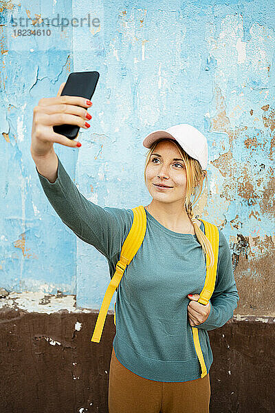 Lächelnde Frau mit Rucksack  die ein Selfie mit dem Smartphone macht