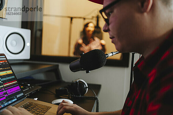 Toningenieur komponiert am Laptop mit Sänger im Hintergrund im Aufnahmestudio