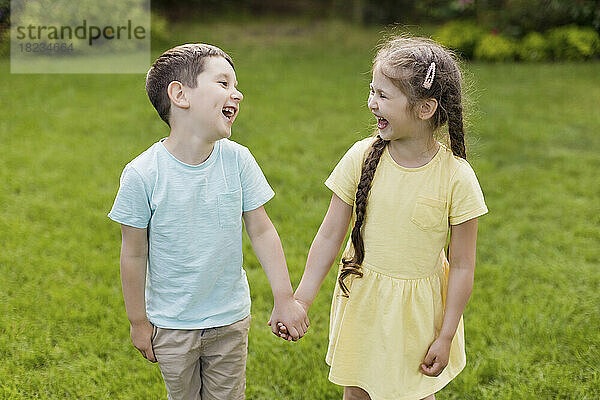 Bruder und Schwester halten Händchen und lachen gemeinsam im Hinterhof