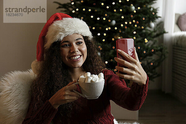 Glückliche Frau mit Weihnachtsmütze und Selfie mit einer Tasse Marshmallow-Kakao