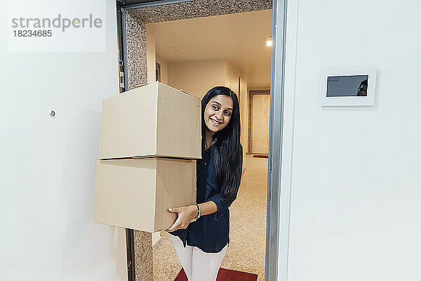 Smiling woman holding boxes walking in home