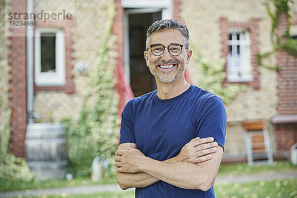 Glücklicher Mann mit Brille und verschränkten Armen im Hinterhof