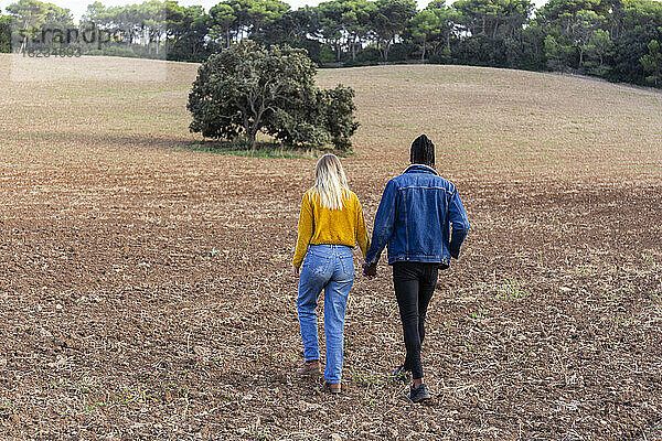 Young man holding hand of girlfriend and walking on field