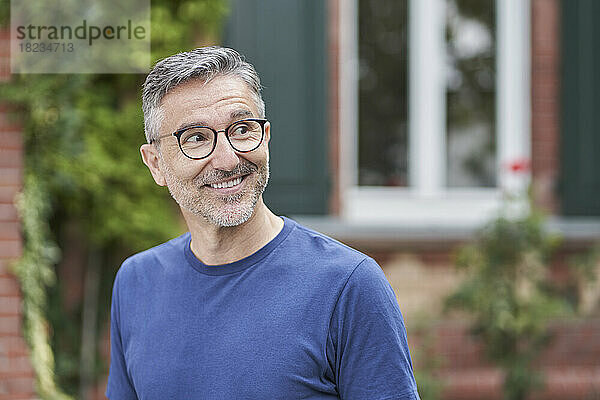 Lächelnder Mann mit grauen Haaren vor dem Haus