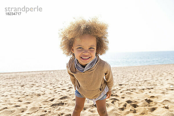 Glückliches süßes Mädchen mit Afro-Frisur  das am Strand steht