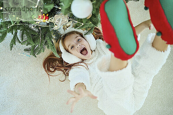 Fröhliches Mädchen liegt zu Hause auf dem Teppich neben dem Weihnachtsbaum