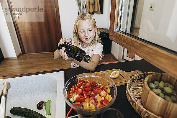Girl preparing a salad in the kitchen pouring oil into bowl
