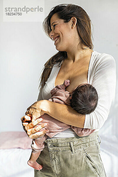 Lächelnde Mutter stillt neugeborene Tochter zu Hause