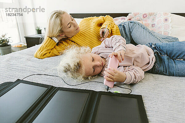 Mutter und Tochter benutzen Smartphones  die im Bett liegen