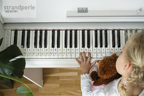 Girl with teddy bear learning piano at home