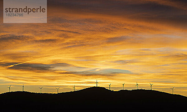 Stimmungsvoller Himmel über den Silhouetten von Windkraftanlagen bei Sonnenuntergang