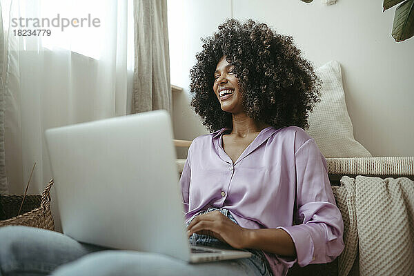 Fröhliche junge Frau mit Laptop im Wohnzimmer