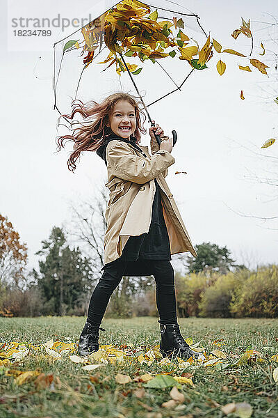 Fröhliches Mädchen  das Spaß mit Regenschirm im Park hat