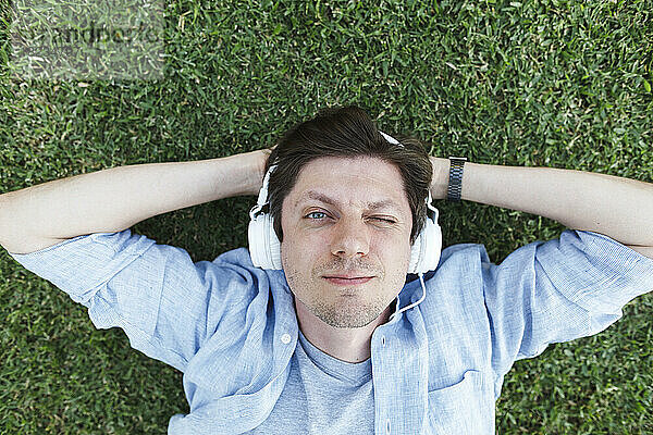Lächelnder Mann  der über Kopfhörer Musik hört und sich im Gras entspannt