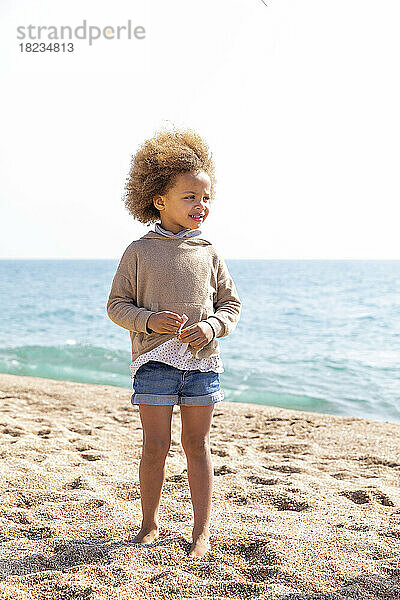 Nettes Mädchen mit Afro-Frisur  das am Strand vor dem Meer steht