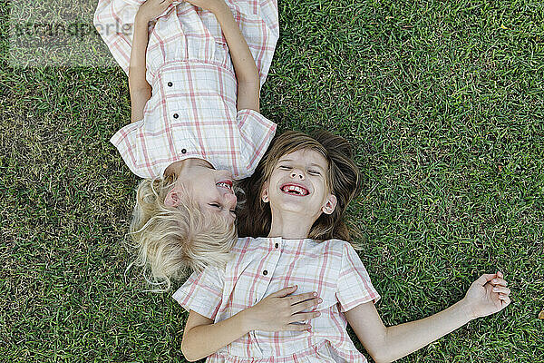 Glückliches Mädchen mit Schwester  die es im Gras genießt