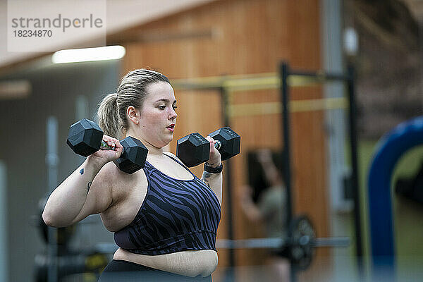 Übergewichtige Frau trainiert mit Hanteln im Fitnessstudio