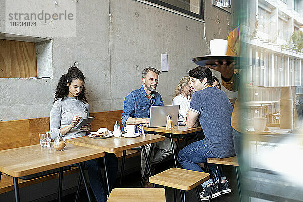 Kunden  die drahtlose Geräte nutzen  sitzen am Tisch im Café