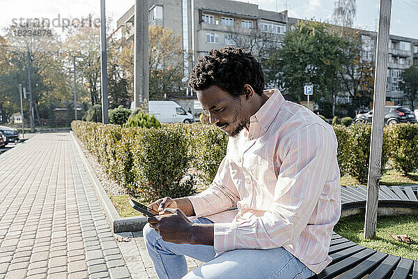 Young man using smart phone sitting on bench
