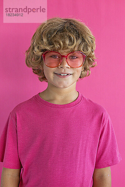 Smiling boy wearing colored sunglasses against pink background