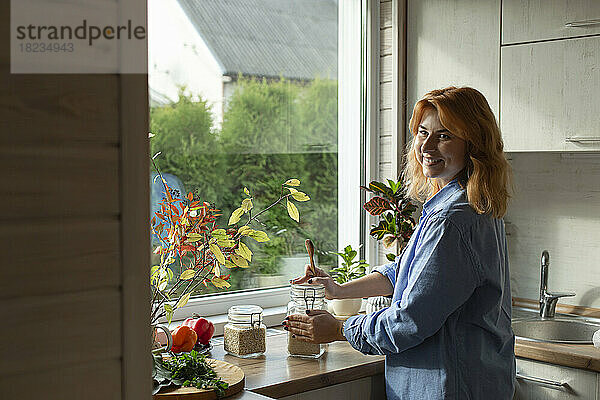 Lächelnde Frau steht in der Küche am Fenster