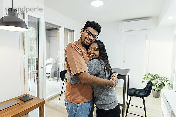 Lächelnder Mann umarmt glückliche Frau im heimischen Wohnzimmer