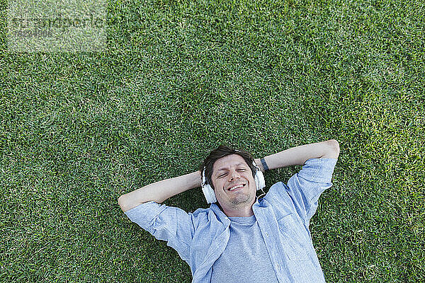 Happy man relaxing in grass and listening to music through headphones