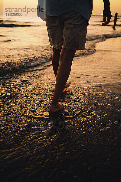 Frau geht bei Sonnenuntergang am Ufer entlang