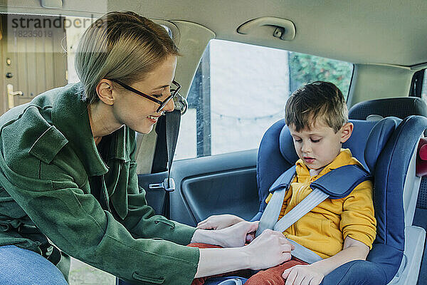 Glückliche Mutter schnallt sich den Sicherheitsgurt über ihrem Sohn an  der im Auto sitzt